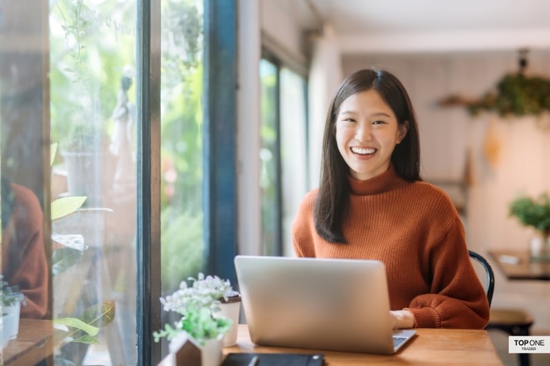 Smiling trader using laptop, representing flexible prop firms with no time limit on evaluations.